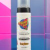 A bottle of tanning mousse sitting on top of a pink tile wall.